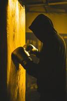 Boxer training with punching bag in dark gym photo