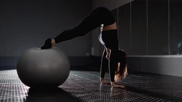 A woman impressively performs a handstand on a stability ball, showcasing her flexibility, strength, and artistry in a minimalistic fitness setting, highlighting the elegance and grace of athleticism video
