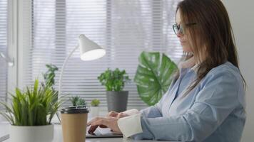 A dedicated woman works at her stylish desk surrounded by greenery, sipping coffee and creating a serene atmosphere that fosters concentration, focus, and creativity for her projects video