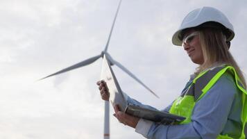 A skilled female wind energy technician analyzes complex data on her tablet next to a towering turbine, highlighting advancements in renewable energy and evolving technology in the field video
