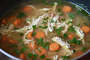 Hot chicken soup with carrots and parsley simmering in pot photo
