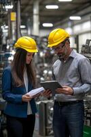 Engineers wearing hardhats discussing factory operations using a digital tablet and paperwork photo