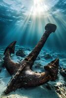 Rusty anchor lying on the seabed with sunbeams shining through the water surface photo
