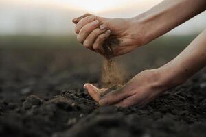 Hands holding and pouring soil on field, symbol of farming, growth, and natural connection. photo