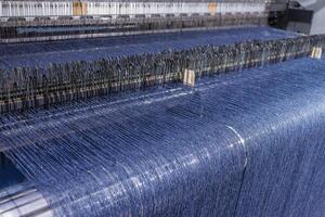 Blue threads on industrial loom weaving fabric in a modern textile manufacturing facility. photo