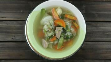 Vegetable soup with cauliflower, meatball, white cabbage, carrots, green peas on wooden background. Rotation display video