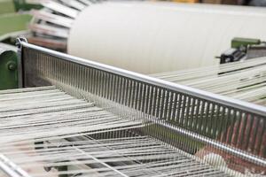 Weaving machine working with white threads in textile production, close-up industrial view. photo