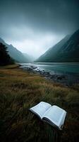 Open book on grass by serene river with misty mountains in background photo