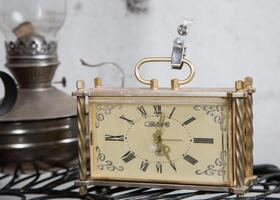 Moscow, Russia, 18.04.2014. A small, ornate clock with Roman numerals sits on a table next to a lantern photo