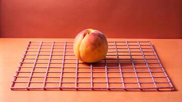 A ripe peach rests atop a coral grid surface. photo
