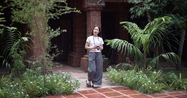 Solo female tourist enjoys taking photos with camera while taking a leisurely stroll amidst serene surroundings and the cultural richness of the place video