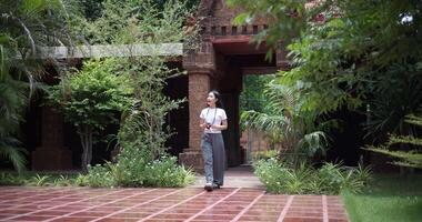 Handheld shot, Solo female tourist enjoys taking photos with camera while taking a leisurely stroll amidst serene surroundings and the cultural richness of the place. Traveling and vacation video