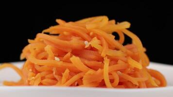 Shredded carrots arranged neatly on a white plate against a black background in a culinary presentation video