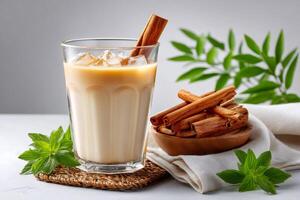 Iced latte with cinnamon sticks and mint leaves is waiting on white table photo