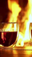 Steaming tea in double-walled glasses glows warmly by the blazing fireplace. Vertical footage video
