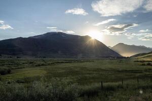 Evening sunlight casts a warm glow over a serene valley surrounded by majestic mountains at sunset photo