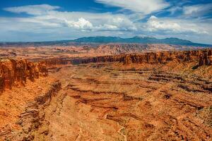 Expansive view of rugged red rock formations under a bright blue sky in a desert landscape photo