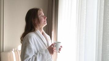 woman waking up, open window curtains and stretching in the morning, drinking hot drink from the cup video