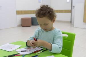 Curly child draws with pencils sitting at the table photo