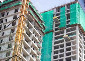 High-rise building under construction with tower crane and green safety netting for worker safety and structural development photo
