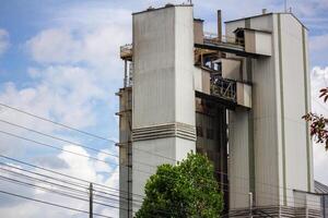 Tall cement plant structure with modern architecture under blue sky, power lines in foreground photo