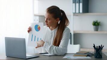 A young woman confidently presents data charts to an unseen audience in a bright, modern office. She is engaged in a discussion about corporate strategies and performance metrics. video