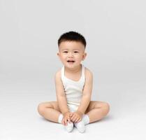 A baby in a white bodysuit sitting on the floor photo