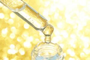Golden liquid droplet falling from pipette into bottle on sparkling background. photo