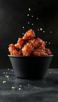 Korean spicy chicken with chili and sesame floating on black paper bowl dark vertical background photo
