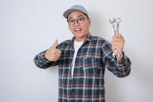 Mechanic holding a wrench while showing thumb up and standing in the studio, isolated on white background photo