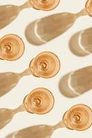 White wine glasses peach color glass on beige background as creative pattern, with beautiful shadows and caustics from sun. Summer light alcohol drinks. Wine glass, top view glassware photo