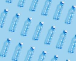 Pattern with blue plastic bottles on blue paper background, top view empty plastic bottle for water half litre, minimal image. Pollution, plastic garbage, environmental protection concept photo
