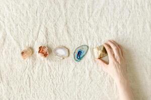 Row of crystals on table, woman hand holding onyx pyramid, healing minerals agate, quartz, amethyst, onyx. Stones for stone therapy, lithotherapy, rock for ritual. Top view, flat lay photo