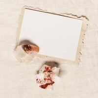 Square invitation card mock up, blank greeting card and protection crystal, healing stone quartz on table. Torn paper. Minimal business brand template. Flat lay, top view, copy space photo