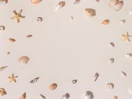 Frame with seashells and starfish with shadow on beige pastel background at sunlight. Summer vacation nautical pattern. Minimal flat lay with natural shell, sea stars, stone. Top view photo
