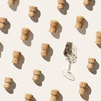 Pattern with champagne corks and wine glass with glitters on beige background, hard light and shadow. Summer wine drinks concept, bottle cap from sparkling wine, repeat pattern top view photo
