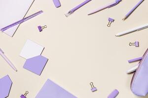 Frame with notebook violet color, pencils, pens, paper clips, pencil case, school stationery flat lay. Back to school concept on beige background, copy space. Office supplies on table photo