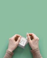 Woman hands open drip coffee bags with ground coffee for brewing in cup, package with paper bag drip coffee filter, mint color background, top view, minimal flat lay, pastel colored photo