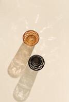 Two glasses of water from colored glass with beautiful shadow and glare at sunlight, summer drink concept, trend glasses orange and black colors on beige, aesthetic top view, caustic effect photo