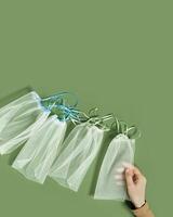 Hand holding reusable grocery bags frm net, reusable packaging for fruits and vegetables, set eco mesh bag with colored ribbon ties, eco friendly and zero waste concept, minimal style photo