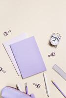 Frame with school stationery very peri trend color, pencils, pens, clips, alarm clock, pencil case. Back to school flat lay on beige background. Office supplies pastel colors on table photo