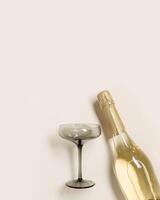Champagne or sparkling wine bottle, champagne glasses from tinted grey glass on beige background. Festive drink minimal concept. Modern wine glasses, grey colored glass. Creative top view, flat lay photo