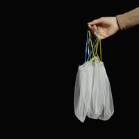 Hand holding empty reusable produce bags, diy from textile, reusable packaging for fruits and vegetables, mesh bag with ties, eco friendly and zero waste concept, black background, side view photo