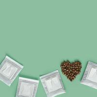 Drip coffee bag and heart from coffee beans, ground coffee for brewing in cup, pack with paper bag drip coffee filter, mint color background, top view, minimal flat lay, pastel color photo