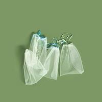 Reusable produce bags, diy organza textile, reusable packaging for fruits and vegetables, mesh bag with ties, eco friendly and zero waste concept, flat lay on olive color background photo