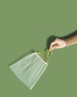 Hand holding reusable produce bags, diy from textile, reusable packaging for fruits and vegetables, mesh bag with ties, eco friendly and zero waste concept, flatlay on olive color background photo