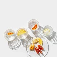 Citrus Infused Water in clear Glasses and plate, artistic light reflections and shadows in natural sunlight. Summer drink concept, minimal pattern, flavored water with yellow red slices of fruit photo