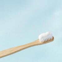 One close up Eco-friendly bamboo toothbrush with white cleansing toothpaste on pastel blue background. Natural wooden material. Sustainable alternative to plastic, zero-waste product for care photo