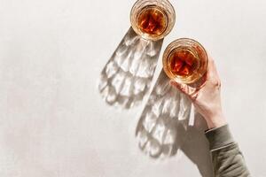 Two Whiskey Glasses with Shadows and sunlight Reflection on beige background, hand holding glass with alcohol, aesthetic top view summer still life, refraction at crystal shine cups, caustics photo