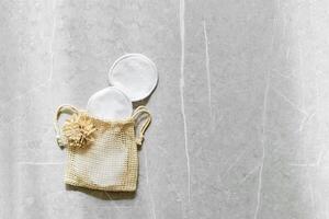 Beige mesh bag with reusable cotton pads decorated dried flower on marble table background, natural light and shadows. Eco-friendly and sustainable beauty routine, self-care and zerowaste concept photo
